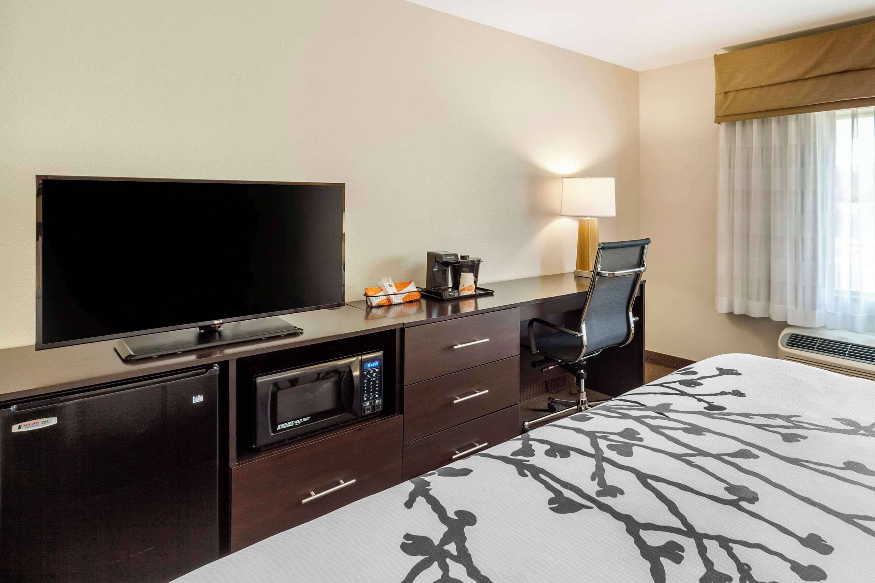 A hotel room with a flat-screen TV, a coffee maker, a microwave, a desk with a chair, and a bed with a patterned bedspread.