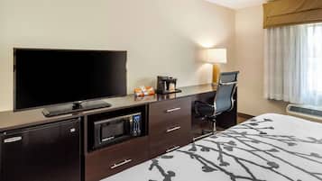 Habitación de hotel con televisión de pantalla plana, cafetera, microondas, escritorio con silla y cama con colcha estampada.