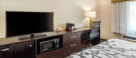 A hotel room with a flat-screen TV, a coffee maker, a microwave, a desk with a chair, and a bed with a patterned bedspread.