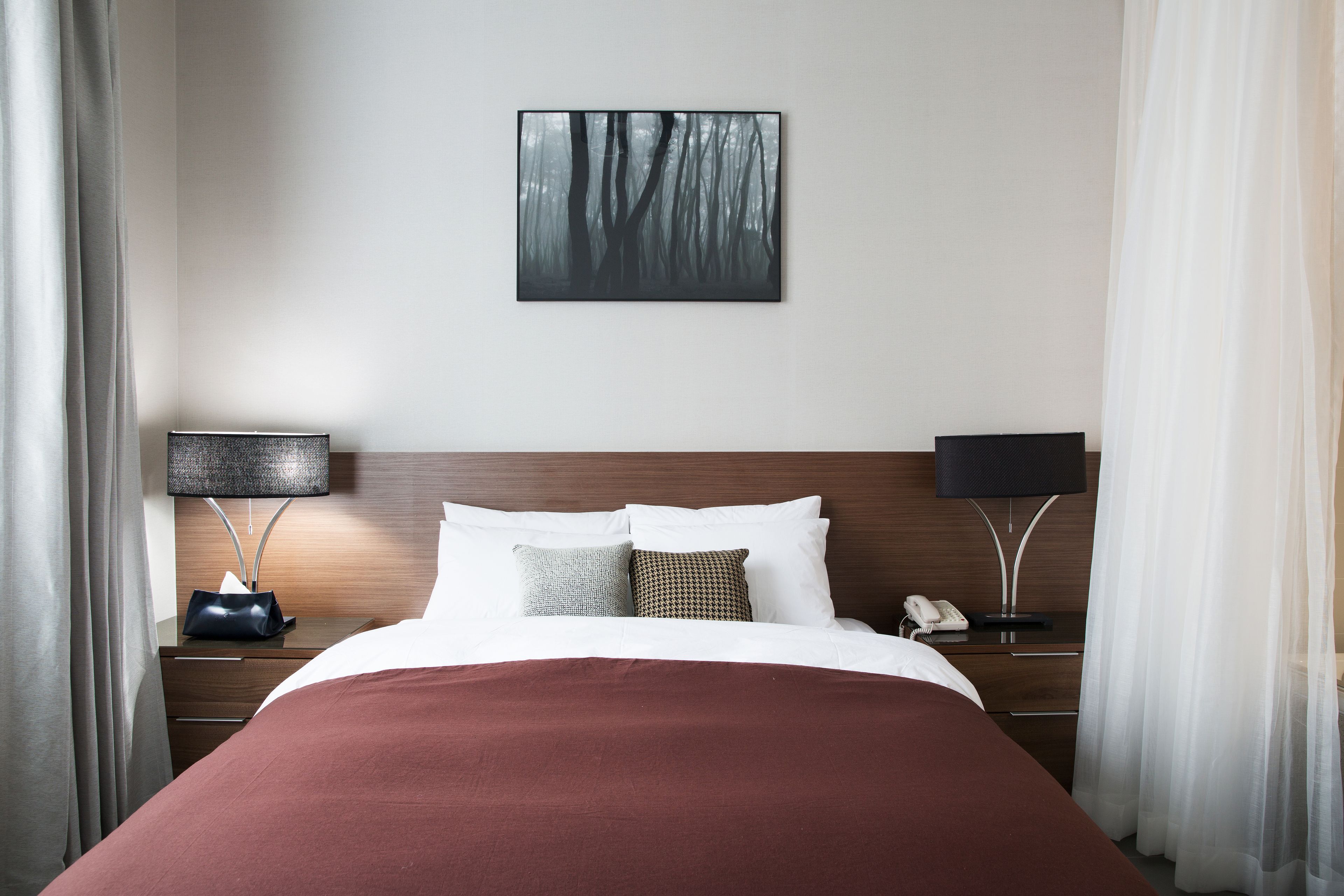 A hotel room with a neatly made bed, a bedside table with a lamp, and a painting on the wall.