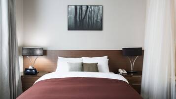 A hotel room with a neatly made bed, a bedside table with a lamp, and a painting on the wall.