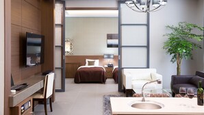 Une chambre d’hôtel moderne avec un grand lit, un bureau avec un ordinateur, une télévision, un lustre, un canapé, une table basse et une plante.