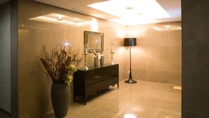 Une salle de bain moderne avec un grand miroir, un meuble-lavabo en bois foncé, une lampe sur pied et un vase contenant des branches séchées.