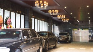 Un hall d’hôtel au design moderne, avec un grand lustre, un comptoir d’accueil et plusieurs voitures garées.