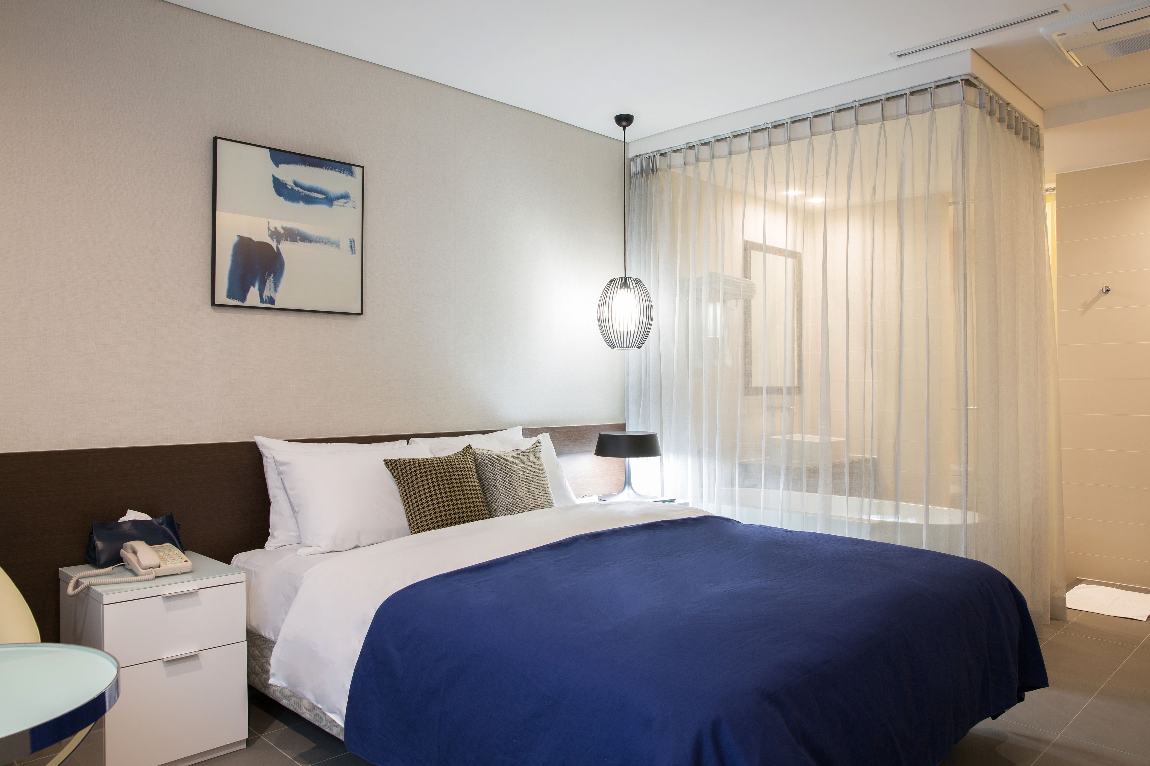 A hotel room with a large bed, a bedside table with a phone, a lamp, and a painting on the wall.