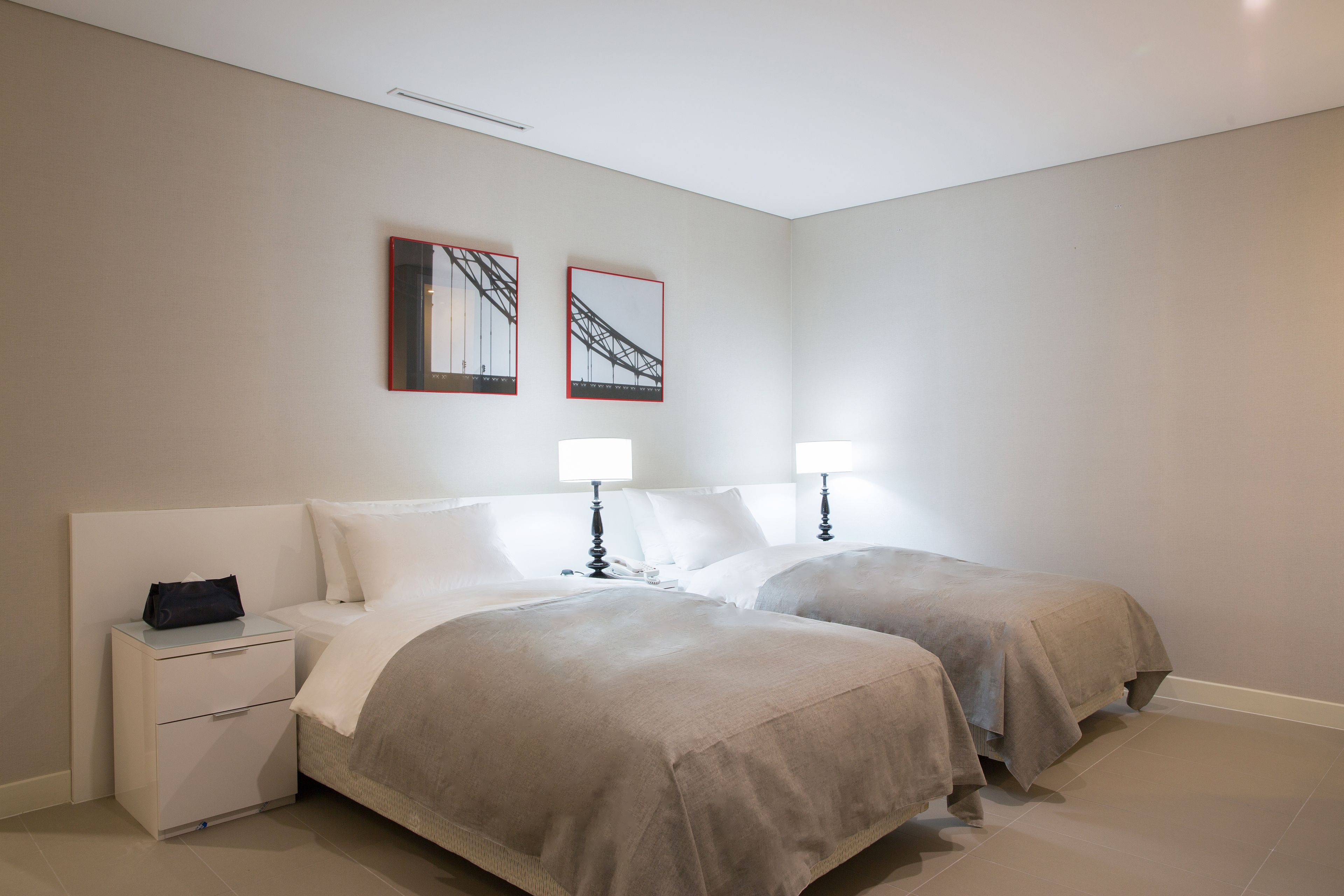 A hotel room with two beds, a nightstand, a lamp, and two framed pictures on the wall.
