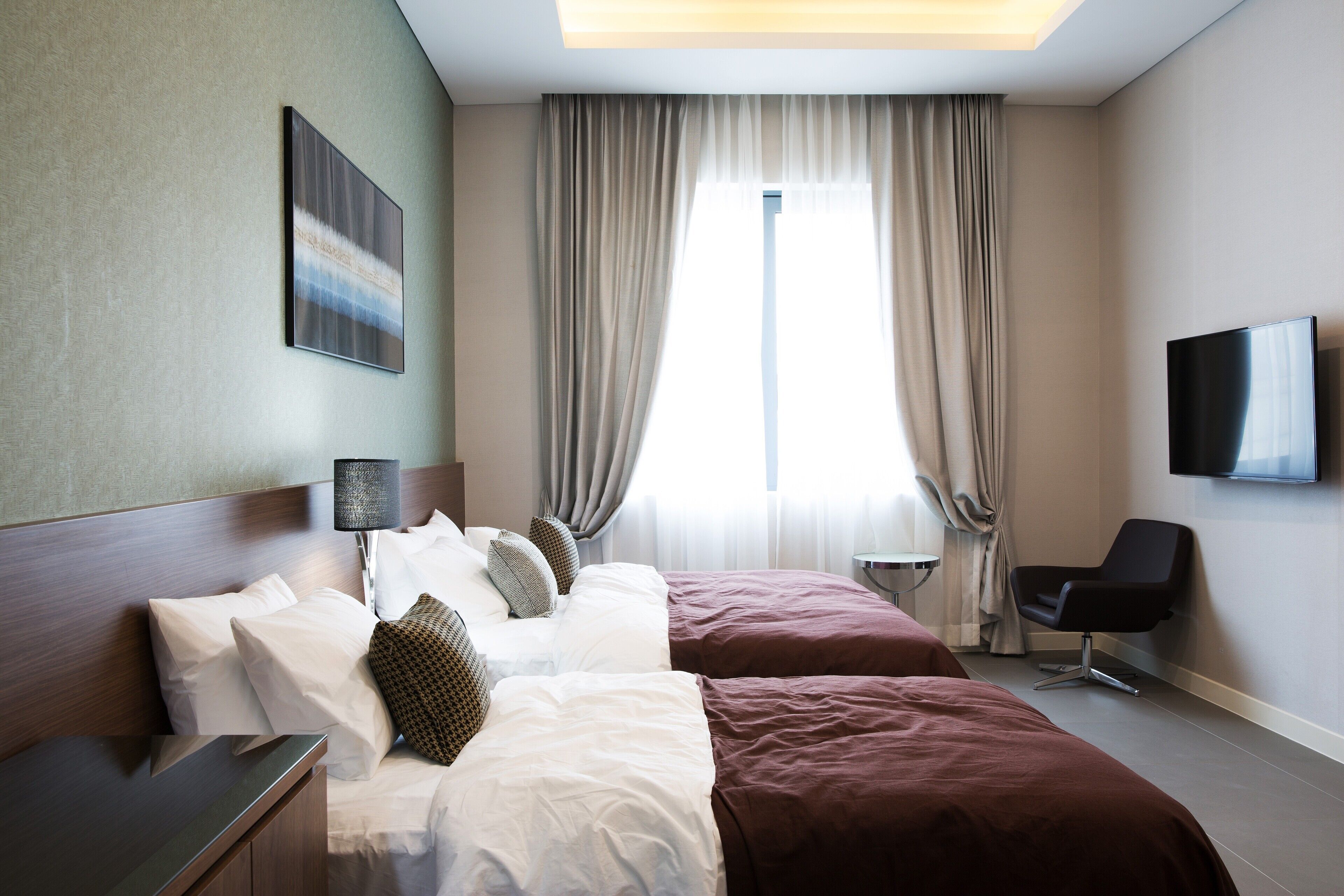 A hotel room with a bed, a desk, a chair, a TV, and a window with curtains.