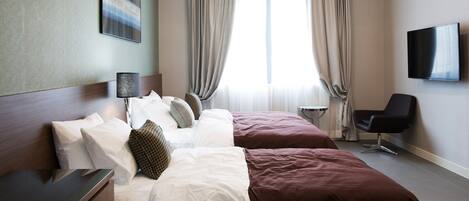 A hotel room with a bed, a desk, a chair, a TV, and a window with curtains.