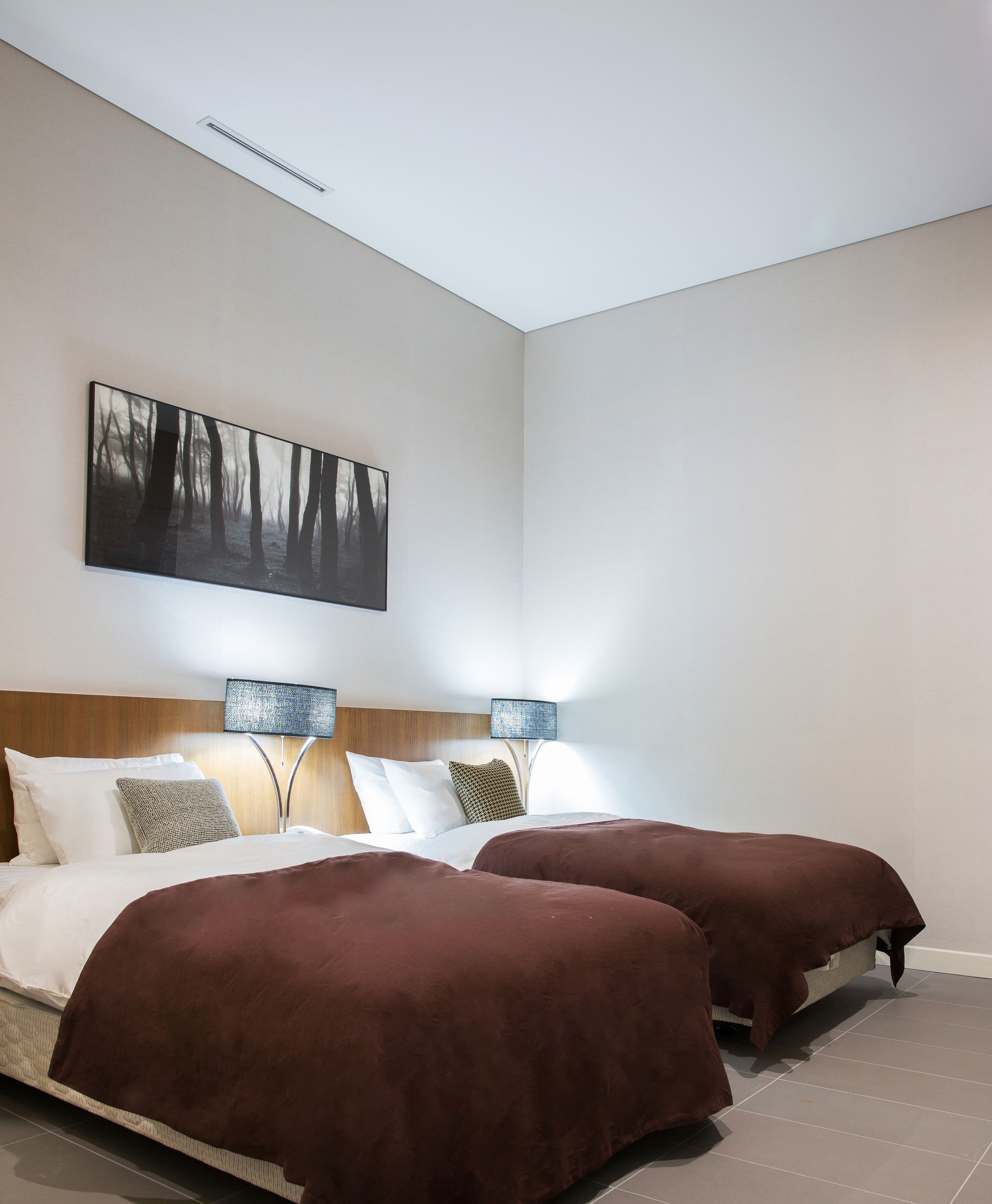 Una habitación de hotel moderna con una cama grande, dos mesitas de noche, un cabecero y una obra de arte colgada en la pared.