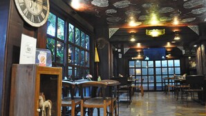 L’intérieur d’un restaurant, avec des meubles en bois, une grande horloge murale et une vue dégagée sur l’extérieur grâce à de grandes fenêtres.
