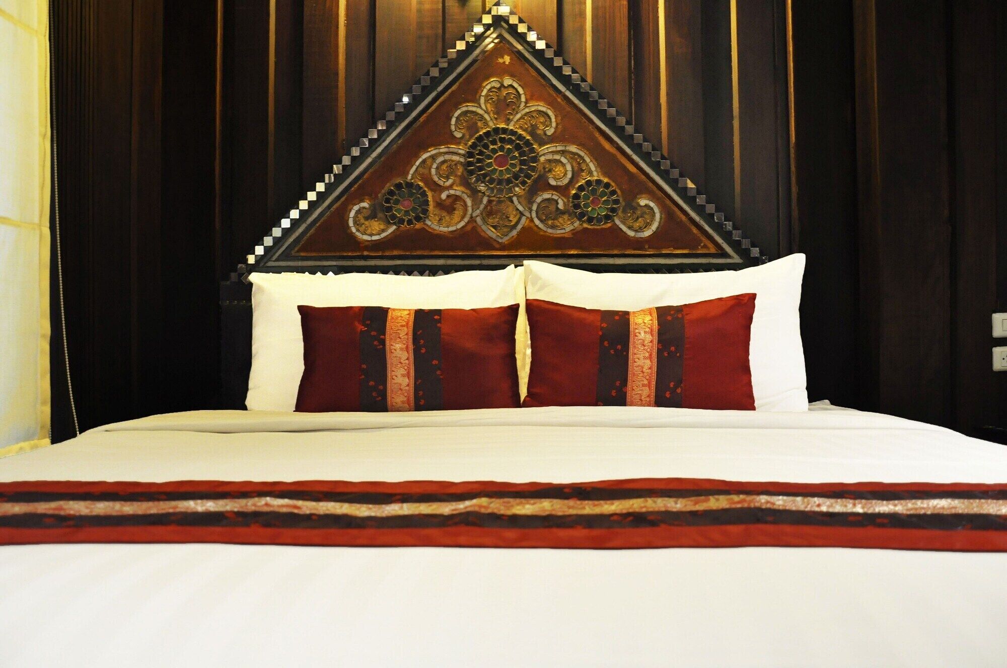 A bed with a decorative headboard, white bedding, and two red pillows with gold accents.