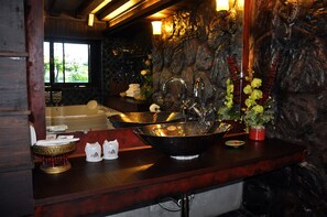 A bathroom with a large black sink, a bathtub, and a stone wall. - Thannatee Boutique Hotel (Chiang Mai)