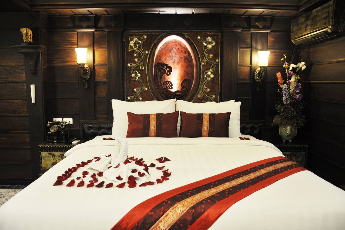 Une chambre d’hôtel avec un grand lit, un miroir décoratif, des appliques murales et un vase rempli de fleurs.