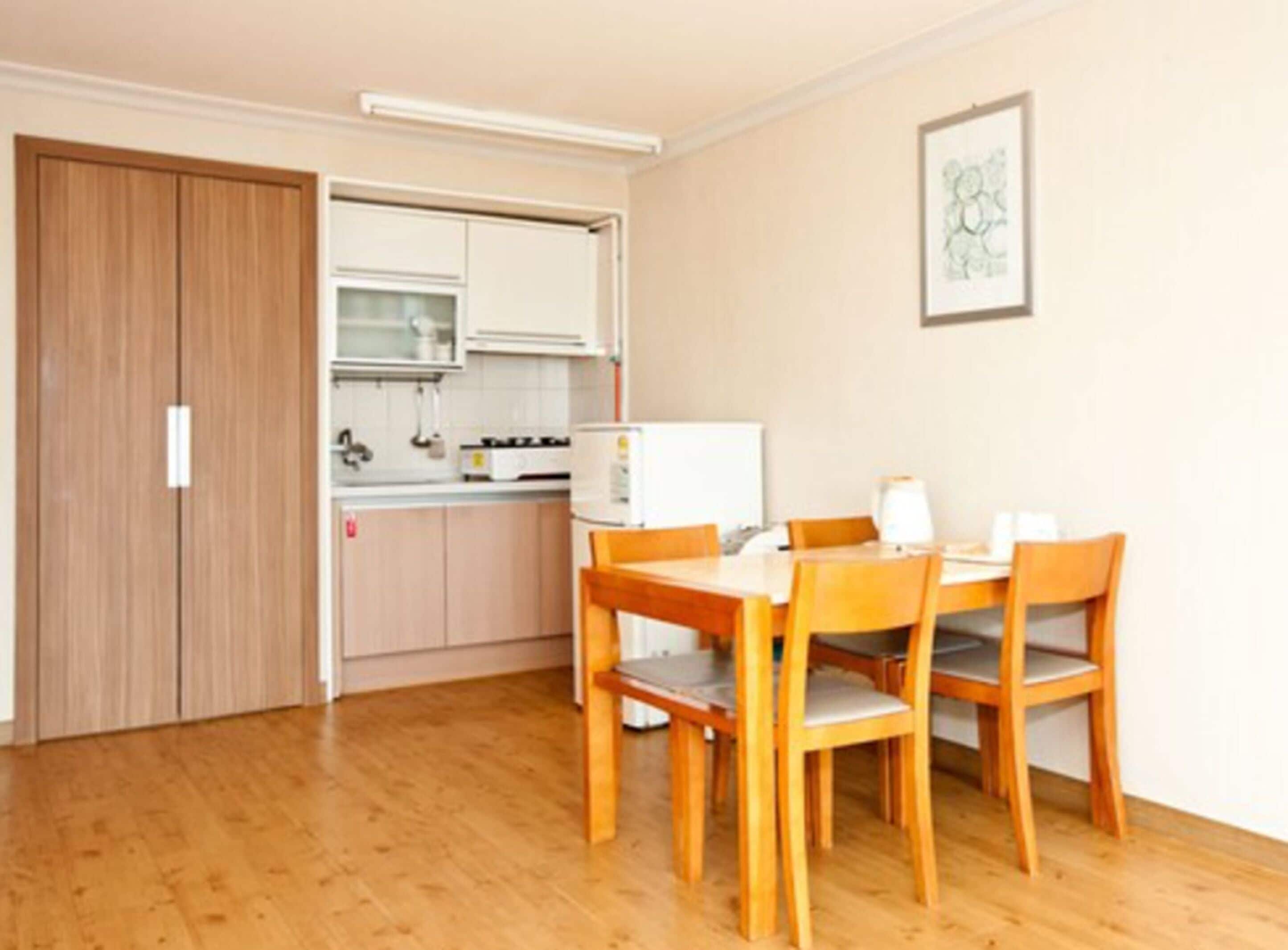 A compact kitchen with wooden cabinets, a white refrigerator, and a dining table with four chairs.