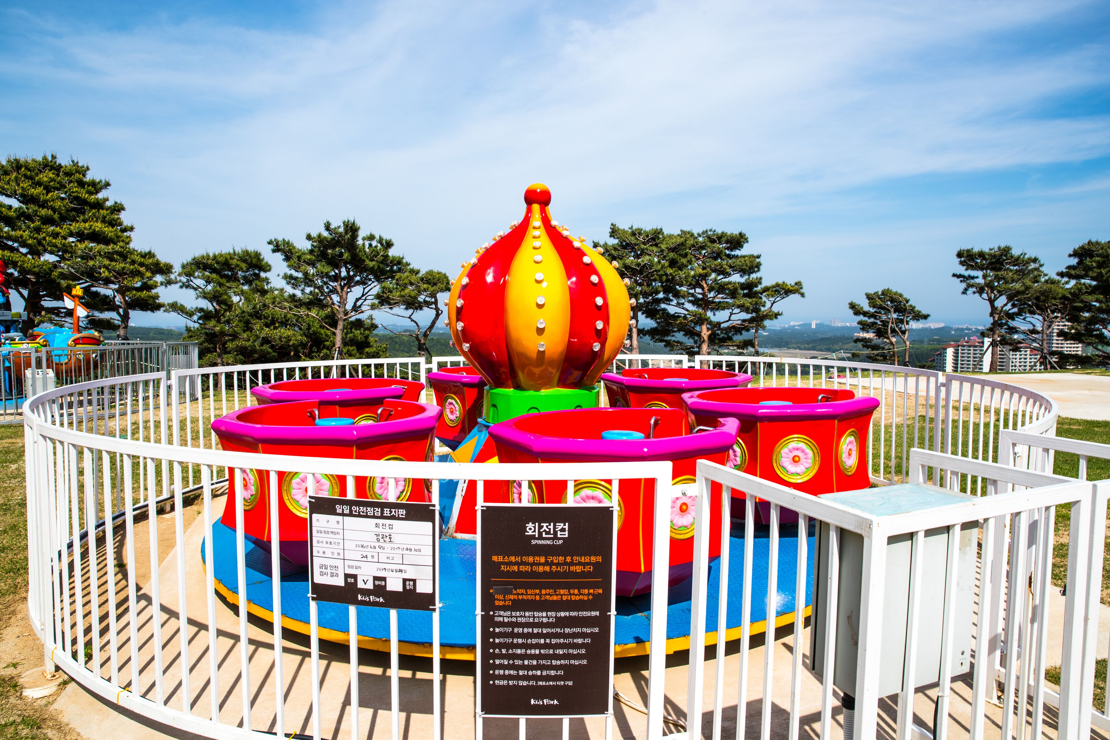 A carousel with a central red and yellow top, surrounded by a white fence.
