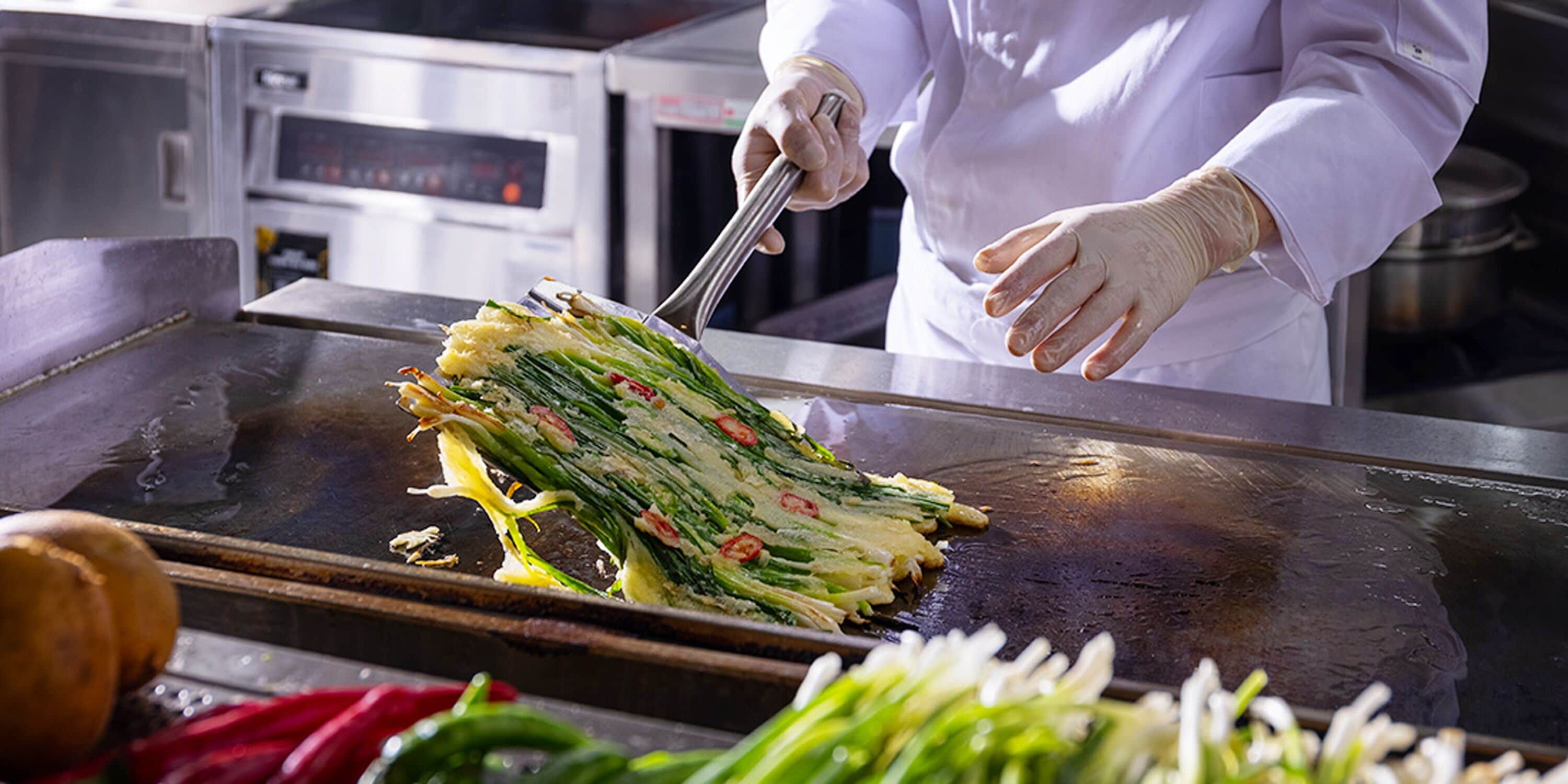Un chef préparant des plats sur une grande plaque de cuisson dans une cuisine professionnelle.