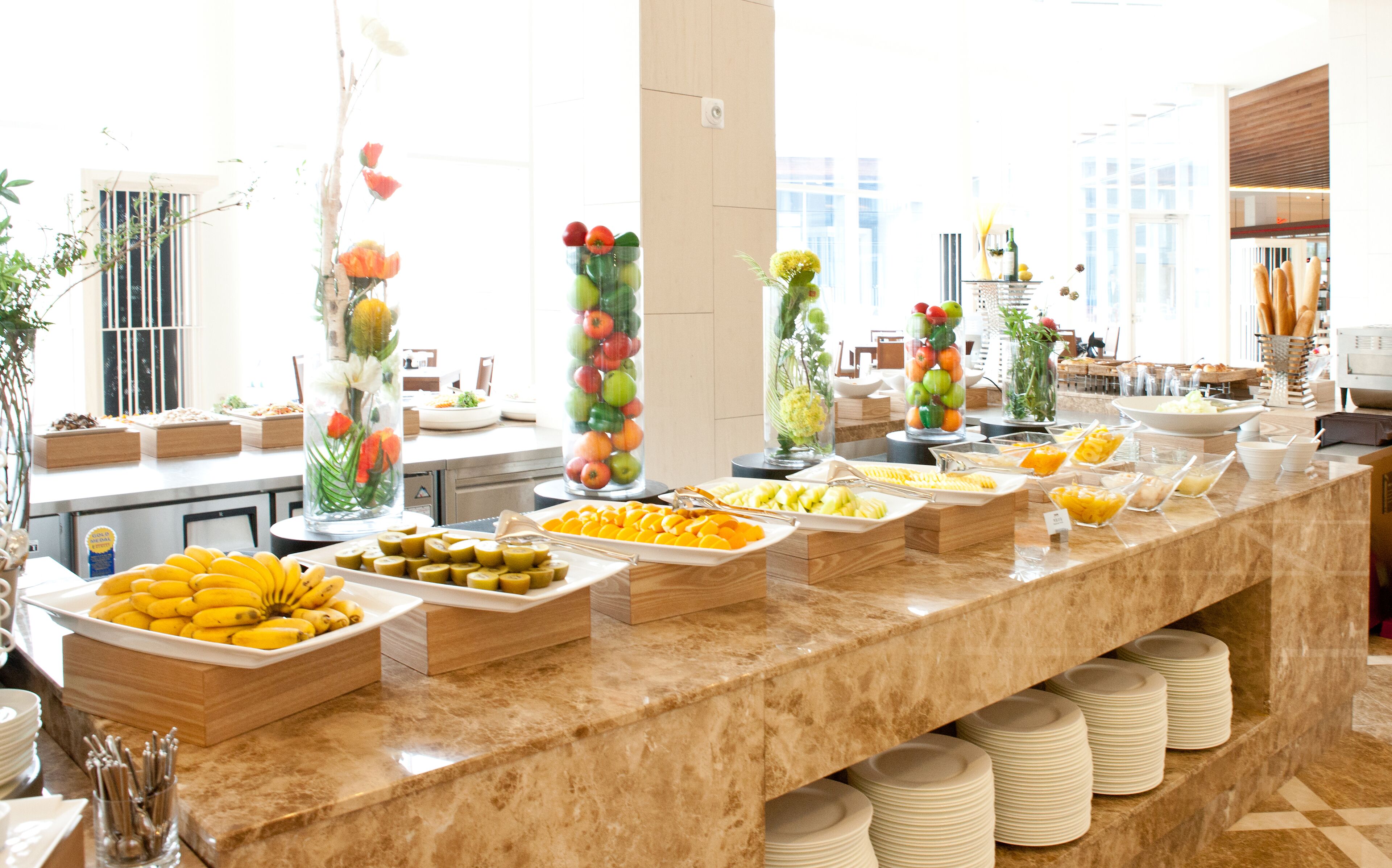 A buffet with various fruits and vegetables, including bananas, oranges, and apples, arranged on a marble counter.