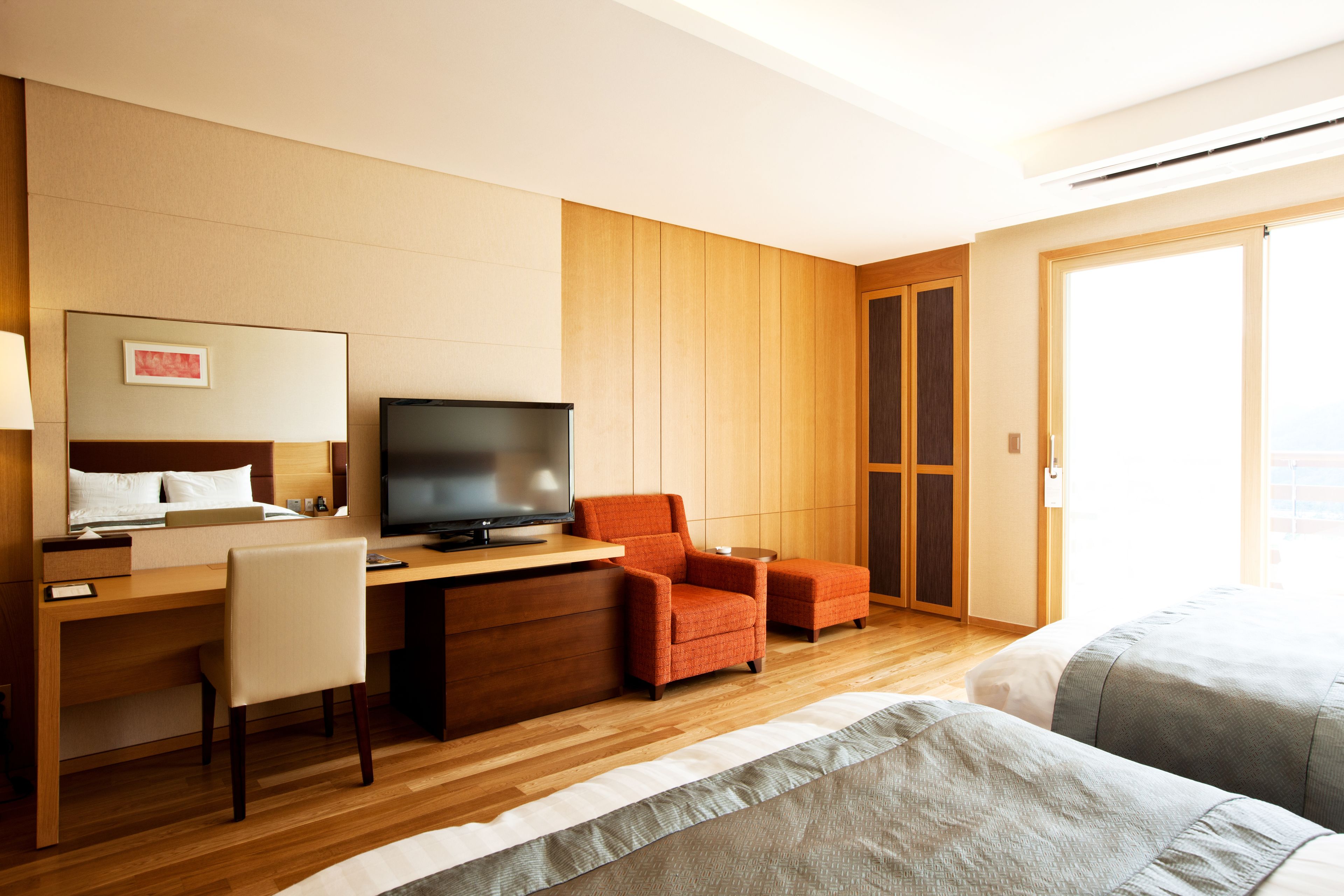 A hotel room with a wooden desk, a television, a bed, and a sliding door to a balcony.