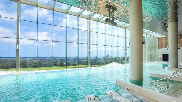 Una piscina interior amb parets de vidre transparent, vistes a l'entorn i una cascada.