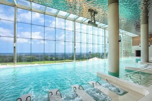 An indoor swimming pool with clear glass walls, a view of the landscape, and a waterfall feature. - Del Pino (Goseong)