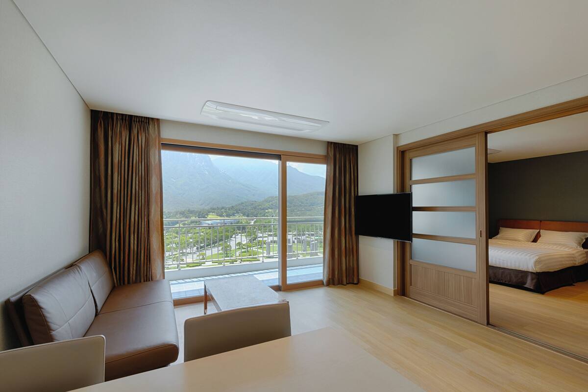 A hotel room with a balcony, a bed, a TV, and a seating area.