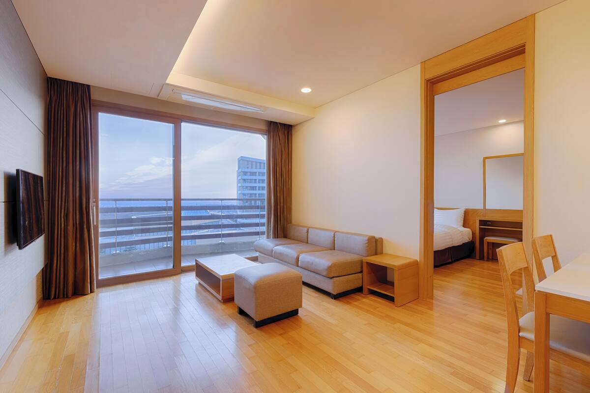 A modern hotel room with a balcony, a sofa, a desk, and a bed.