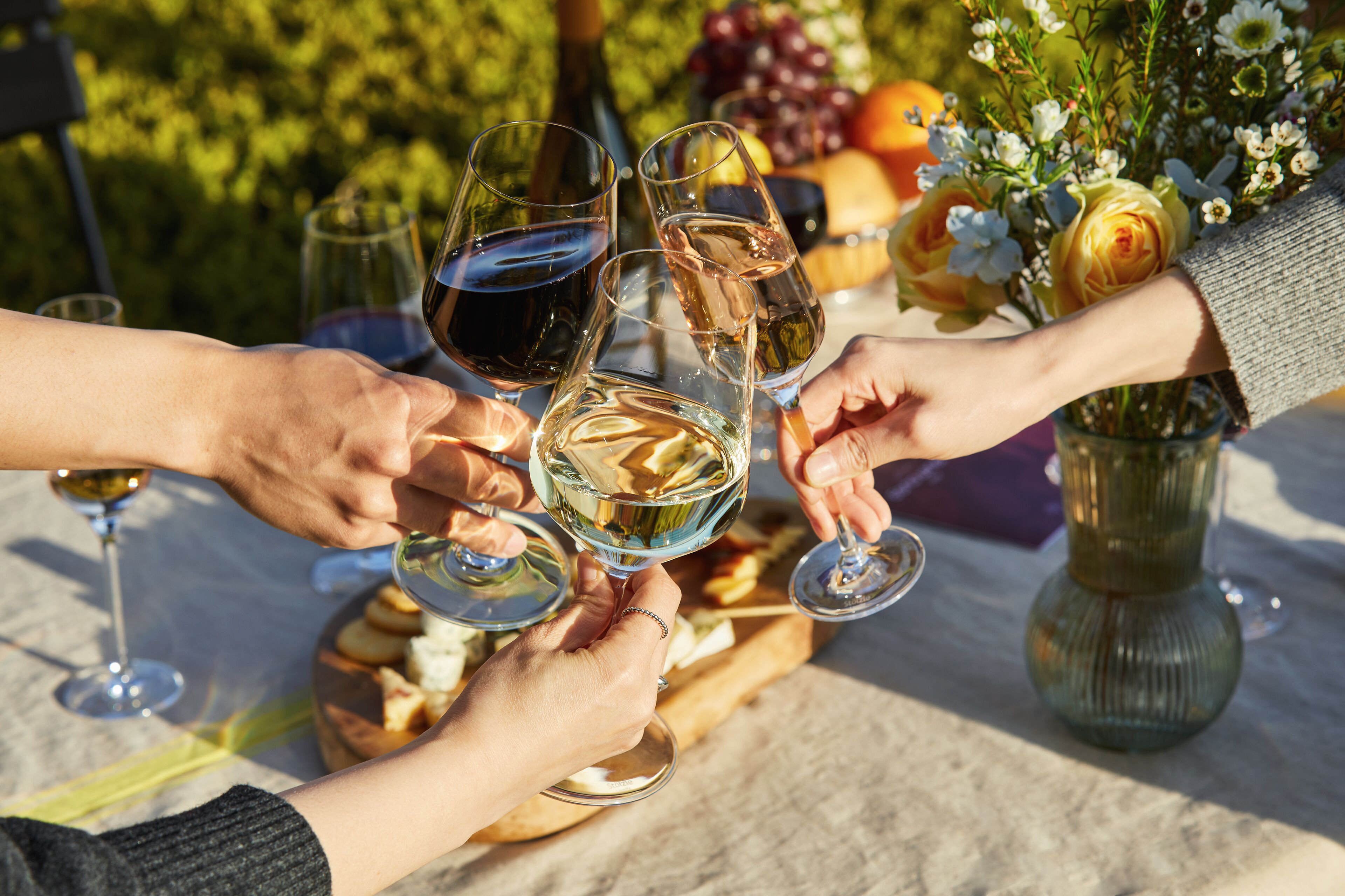 A group of people toasting with wine glasses at an outdoor table with a fruit basket and flowers.