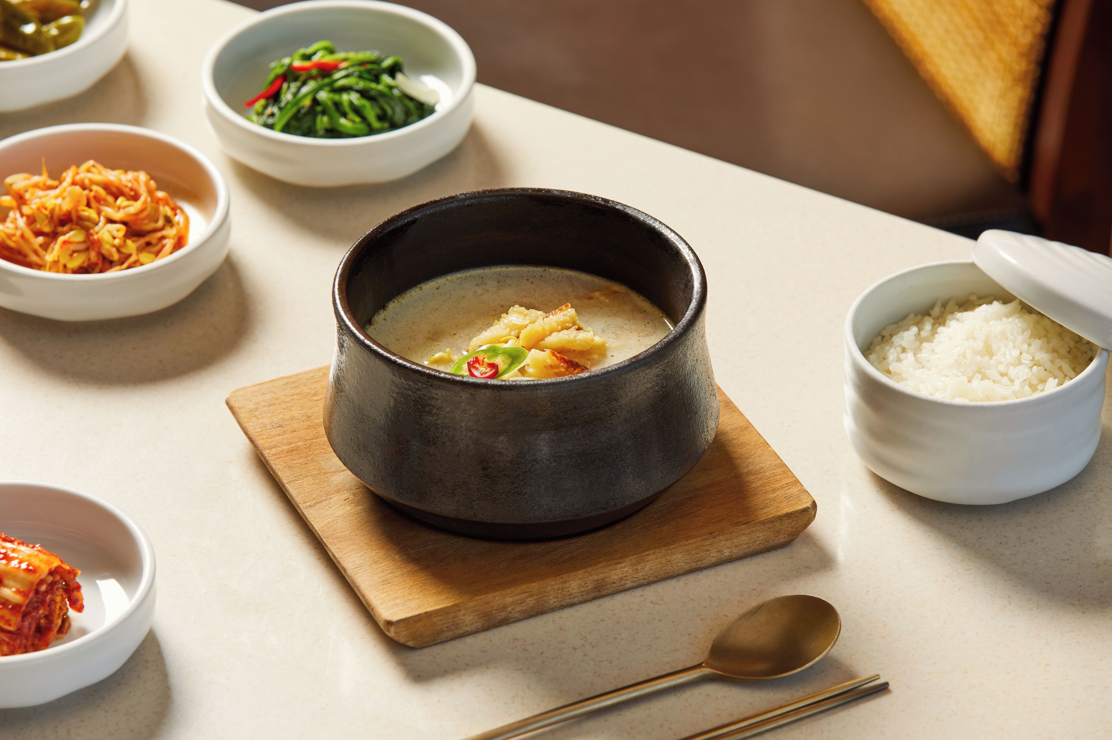A table with various dishes, including a bowl of soup, a bowl of rice, and several side dishes.
