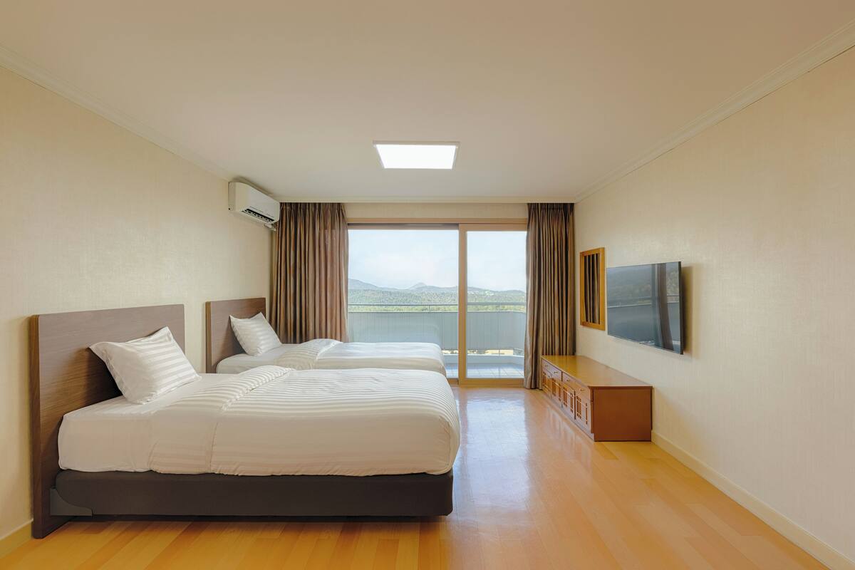 A hotel room with two beds, a TV, and a balcony with a view.