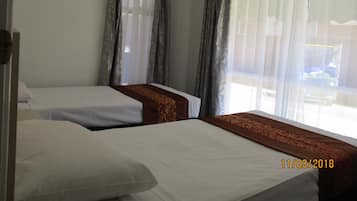 A hotel room with two beds, a window with sheer curtains, and a view of the outside.