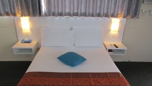A hotel room with a single bed, two bedside tables, a nightstand, a blue pillow, and a brown decorative bedspread. - Cronulla Motor Inn (Cronulla)