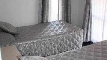 A room with two beds, each with a patterned quilt, a window with curtains, and a door on the left.