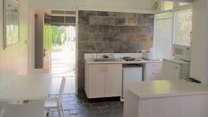 A compact kitchen with a stone backsplash, a built-in microwave, and a window with blinds. - Cronulla Motor Inn (Cronulla)
