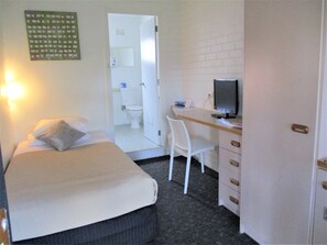 Une petite pièce, de taille modeste, comprenant un lit, un bureau avec un ordinateur et une chaise. Une porte donne accès à une salle de bain.