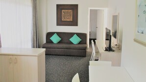 A hotel room with a sofa, a TV, a painting, and a mirror. - Cronulla Motor Inn (Cronulla)