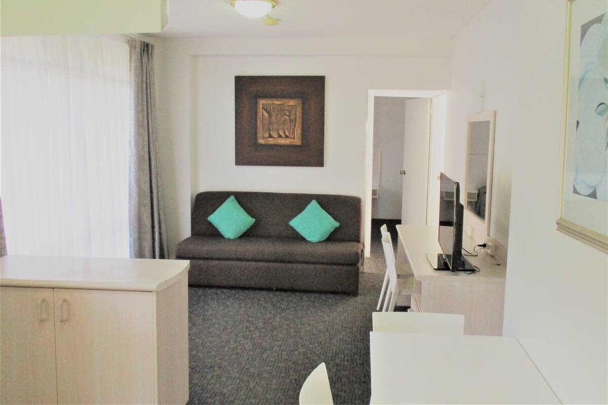 A hotel room with a sofa, a TV, a painting, and a mirror.