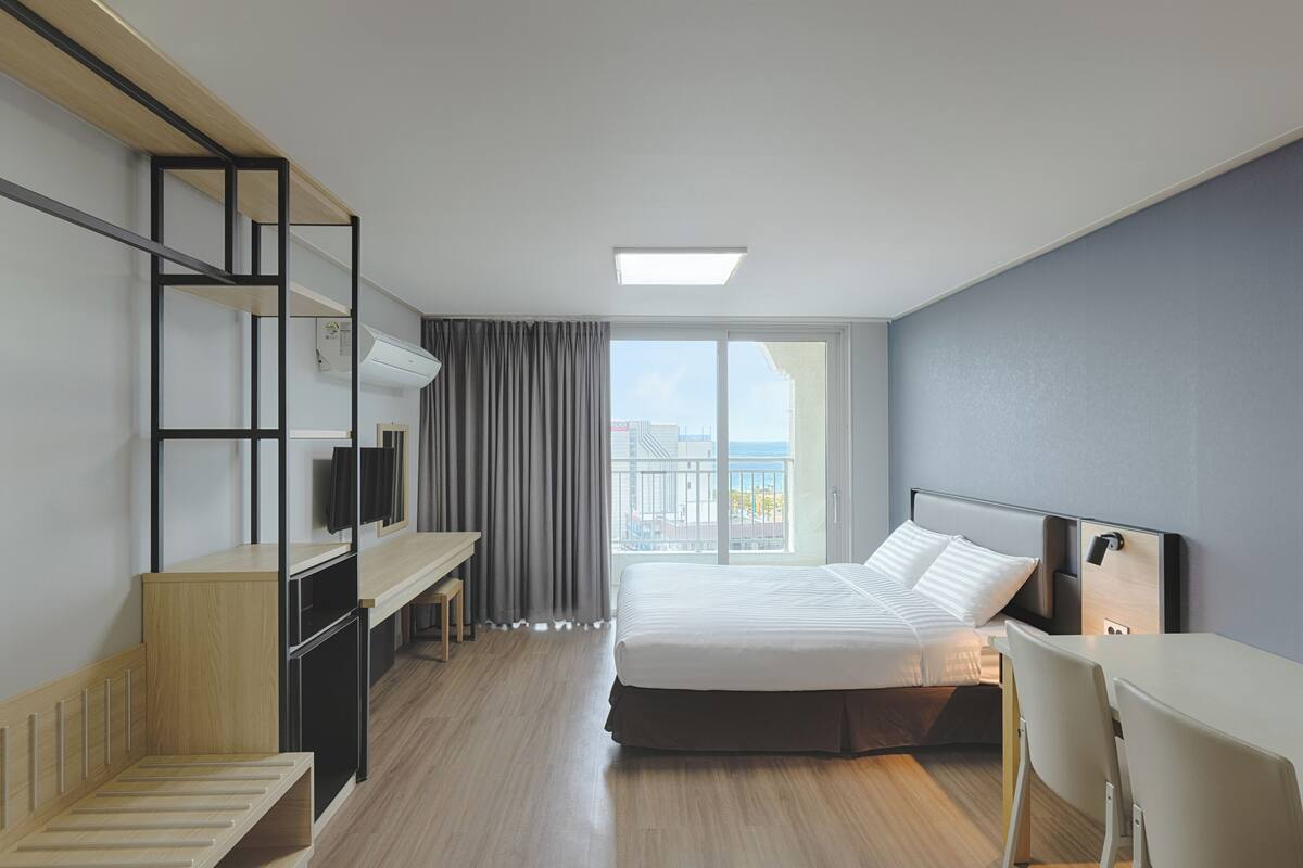 A modern hotel room with a bed, desk, and a view of the city.