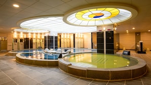 Une grande piscine intérieure dotée de plusieurs couloirs, entourée de chaises longues et agrémentée d’un design de plafond moderne.