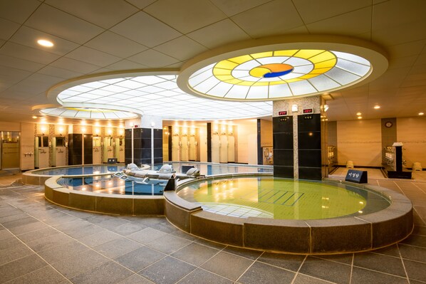 Una amplia piscina cubierta con varias pistas de natación, rodeada de sillones de descanso y un diseño moderno del techo.