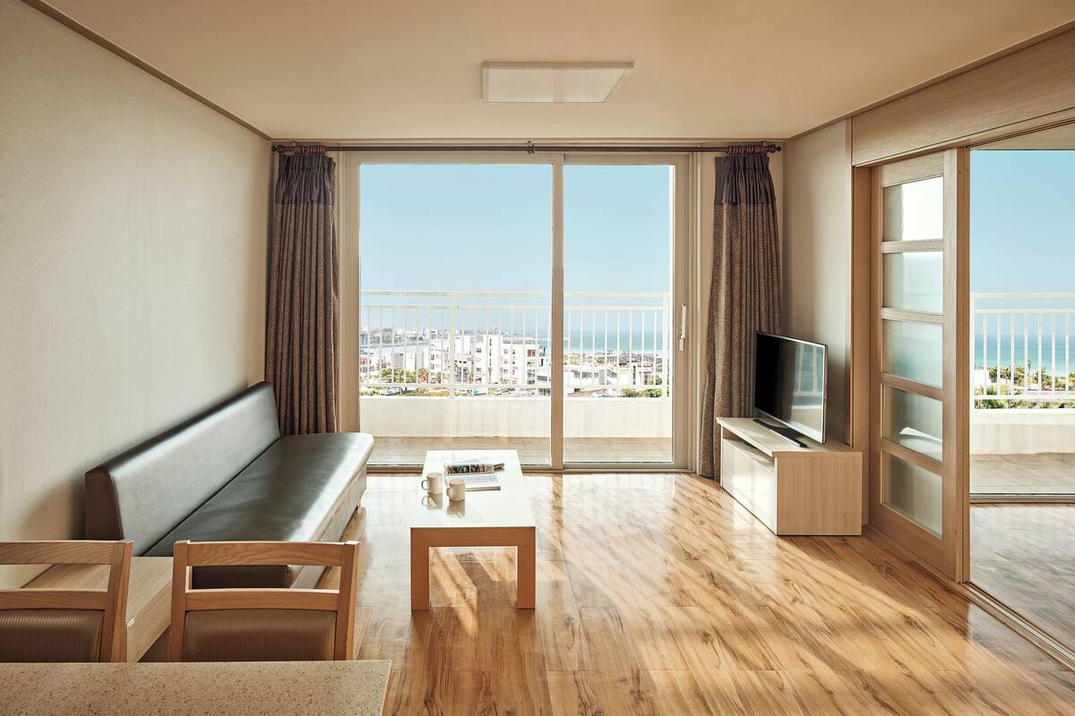 A modern living room with a sofa, coffee table, TV, and a balcony with a city view.