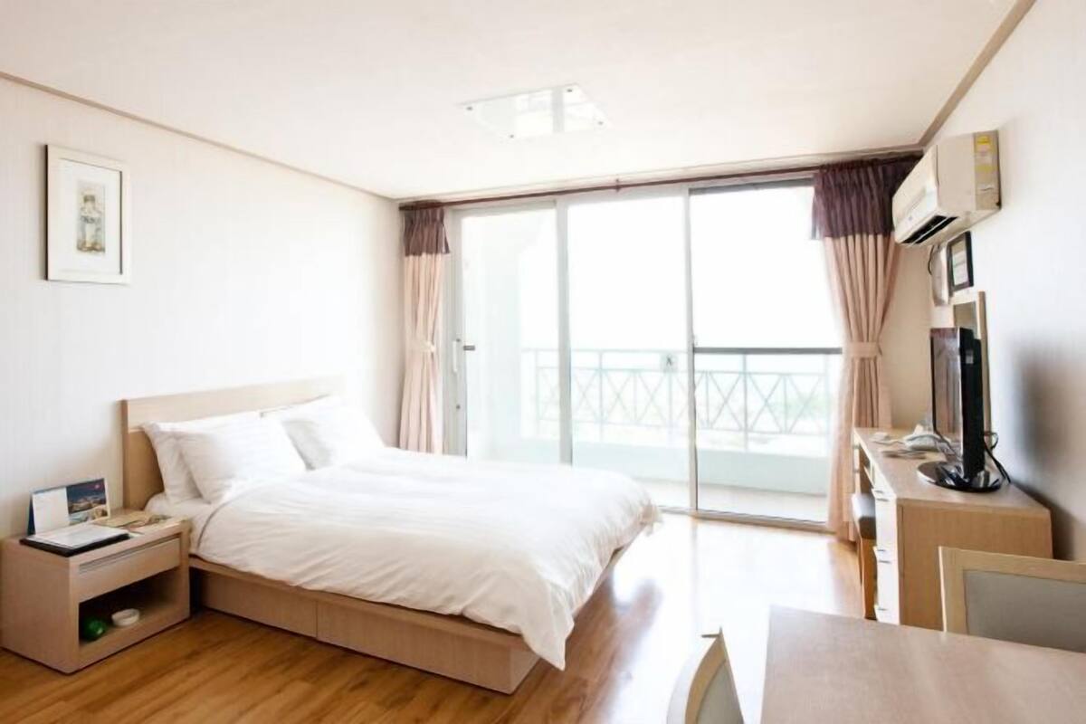 A hotel room with a bed, bedside table, TV, and a balcony with curtains.