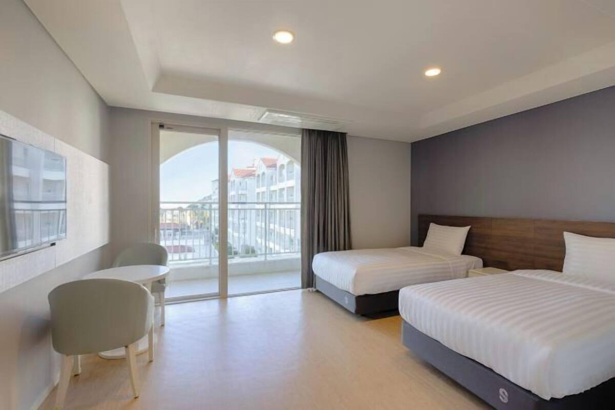 A hotel room with two beds, a dining table, and a large window with a view of buildings.
