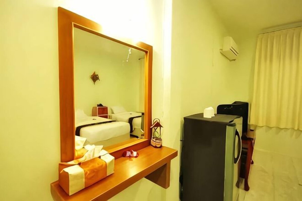 Una habitación de hotel con una cama, una mesita de noche con lámpara, un espejo y un televisor.