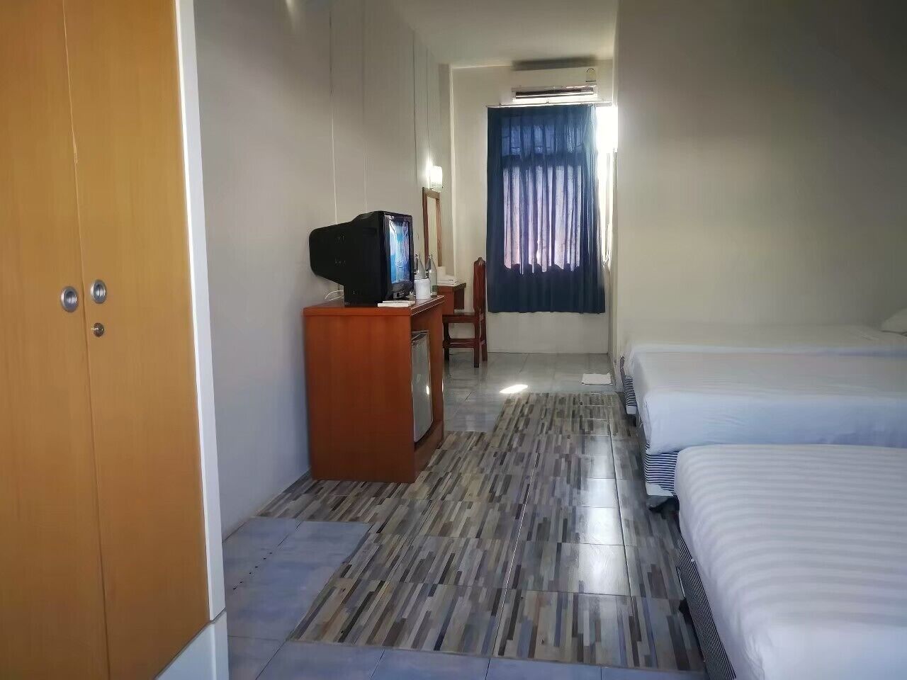 A hotel room with a bed, a desk with a television, a wardrobe, and a bathroom with a shower curtain.