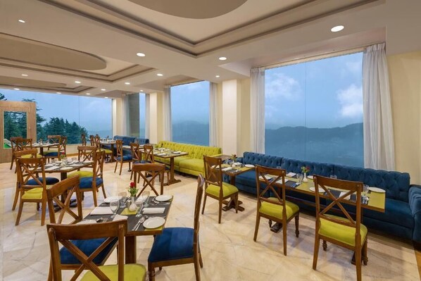 A dining area with tables and chairs, a blue sofa, and a view of the mountains.