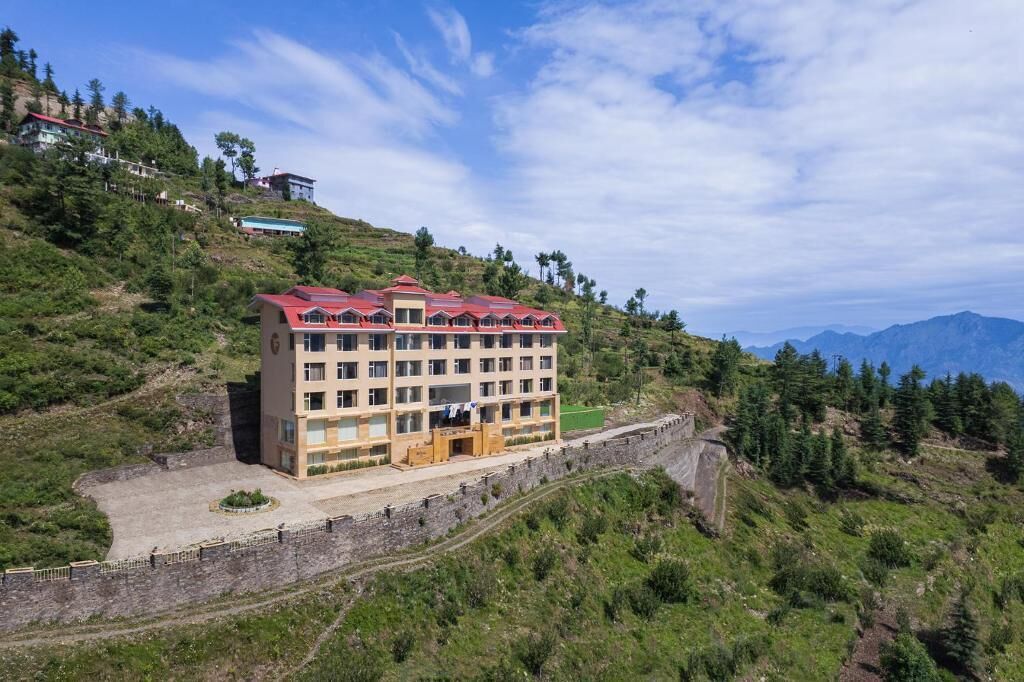 Un hotel de varios pisos con techo rojo, ubicado en una colina con vista a las montañas.