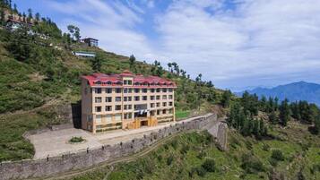 Un hotel de varios pisos con techo rojo, ubicado en una colina con vista a las montañas.