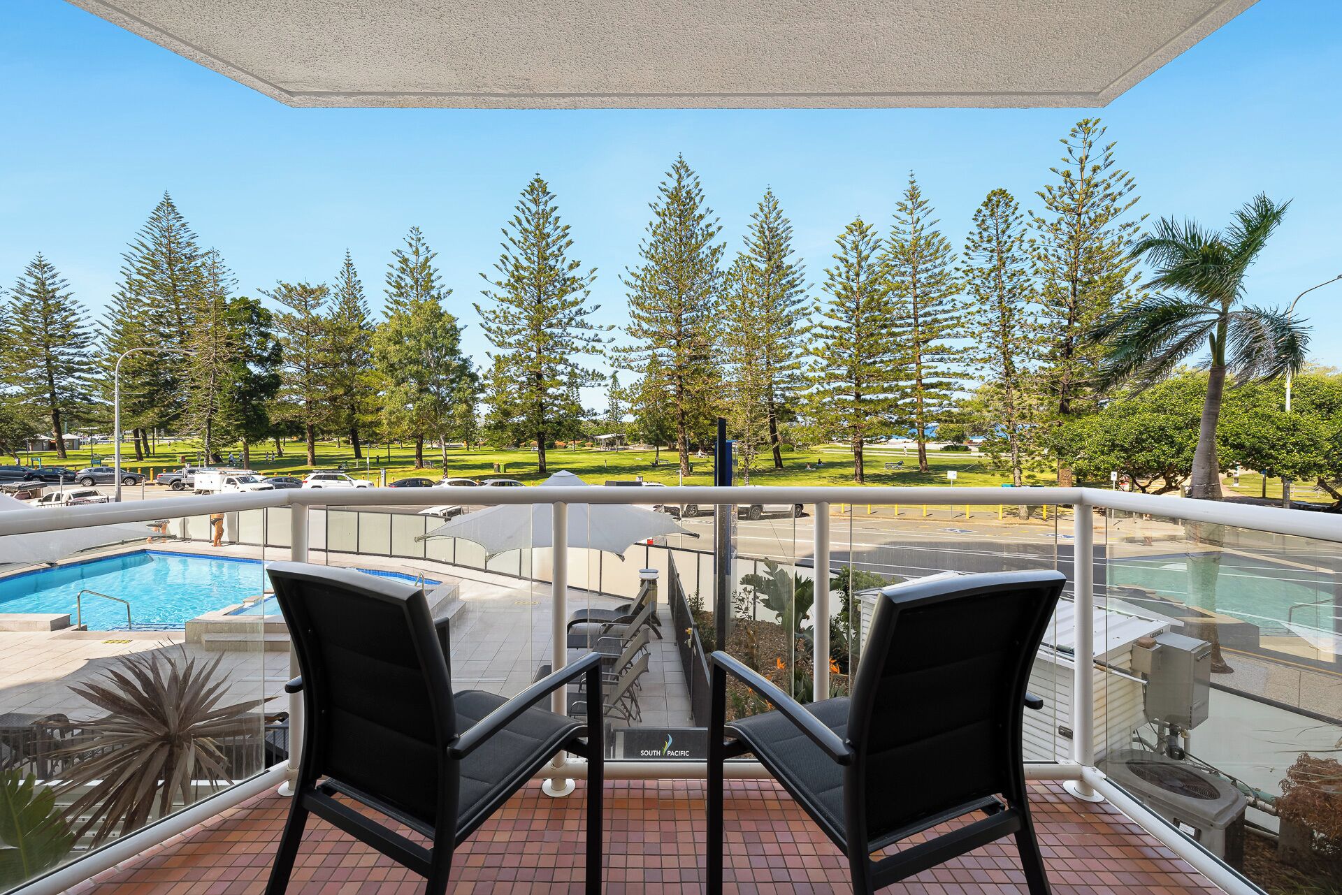 Ein Balkon mit zwei Stühlen mit Blick auf einen Swimmingpool und einen Golfplatz.