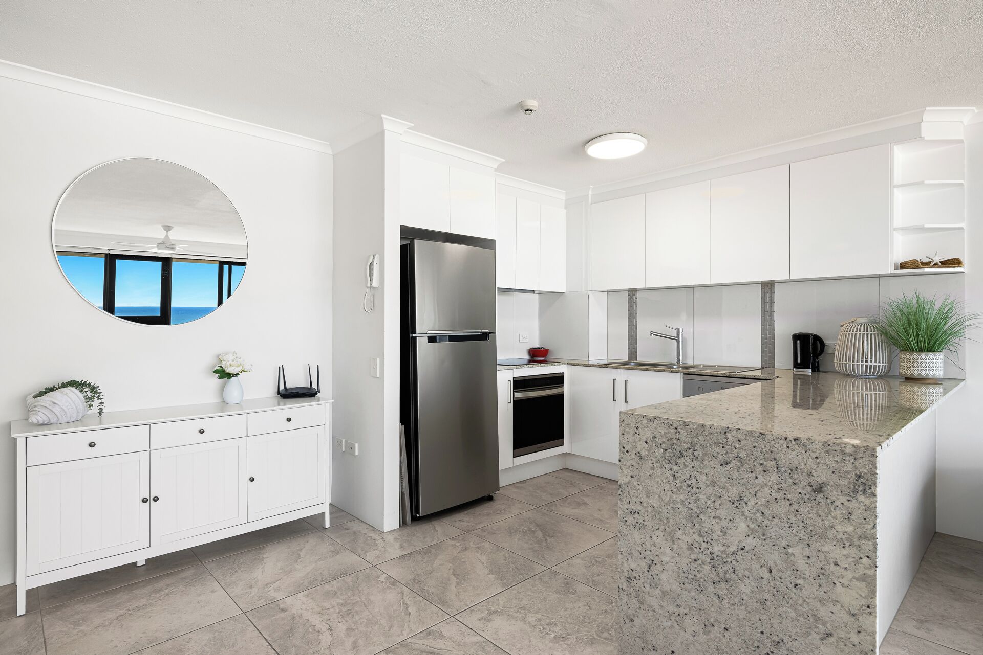 Una cocina moderna con muebles blancos, un refrigerador de acero inoxidable, horno empotrado y encimera de granito.