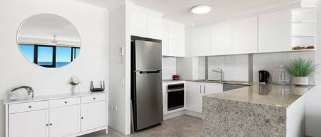 Una cocina moderna con muebles blancos, un refrigerador de acero inoxidable, horno empotrado y encimera de granito.